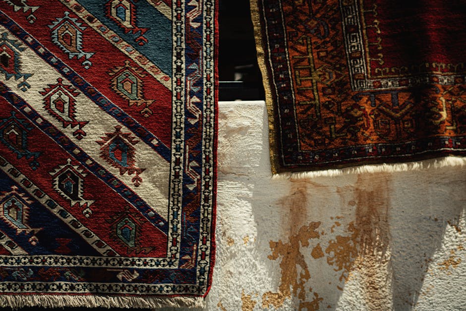 A living room corner featuring an ornate area rug with intricate floral and geometric patterns in shades of orange, beige, and dark blue, covering a wooden floor. To the left, part of a beige upholste